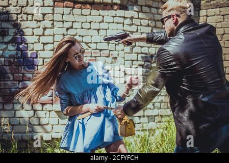the robber on the street threatens the girl with a pistol and wants to take her bag from her. Stock Photo