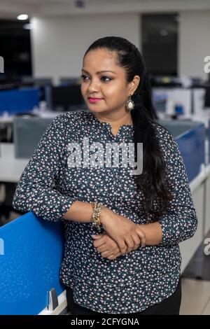 Portrait of young successful Indian business woman with her arms crossed, standing against office background, Stock Photo
