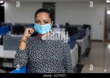 Portrait of successful Indian business woman wearing Covid protection mask and standing against office background, Corporate environment. Stock Photo