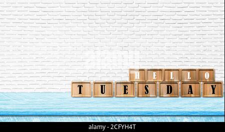 Hello Tuesday alphabet letters put on blue table with white brick wall background. Copy space for text. Stock Photo