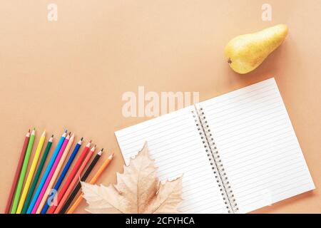 School supplies, notepad, pear and autumn leaf on light brown background. Back to school concept. Top view, flat lay, copy space. Stock Photo