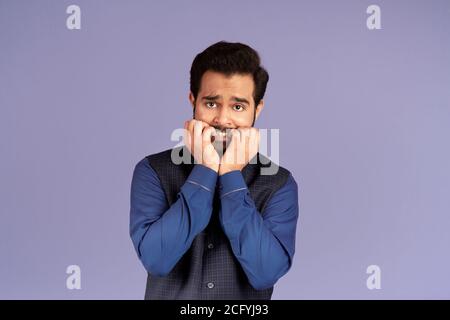 Terrified Indian man biting his nails in panic over lilac background Stock Photo