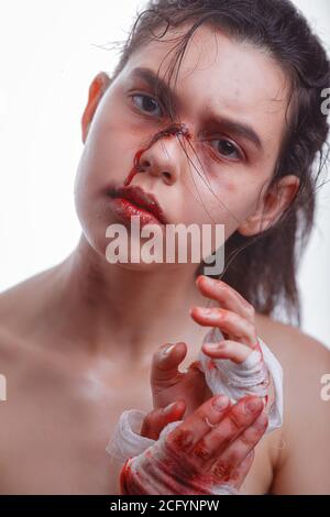 young woman with bruises on face victim of domestic violence. female fighter wearing bloody bandage on her fists, ready to fight. The idea of independ Stock Photo