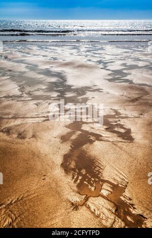 Glistening sand rivulets form abstract patterns on the beach. Stock Photo