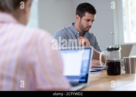 Business Couple Working From Home Sitting At Table During Pandemic Lockdown Stock Photo