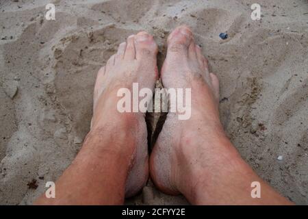 Feet on a sandy beach are covered with sand Stock Photo