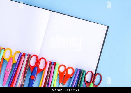 School supplies. Back to School design elements. Colorful markers and scissors on opened empty notepad on light blue paper background. Stock Photo