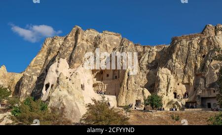 Foreign tourists visiting fabulous natural park with carved rock christian church from volcanic tuff formation in Cappadocia, Turkey. Stock Photo
