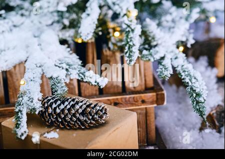 Decorative handmade winter holidays gift box with pine cone and christmas tree covered with artificial snow and lights Stock Photo