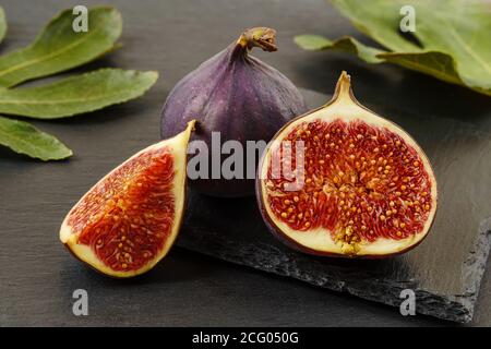 Whole, half and quarter of fresh ripe fig fruits on a black slate background. Sweet fruits and berries. Vegetarian, raw food diet and healthy eating. Stock Photo