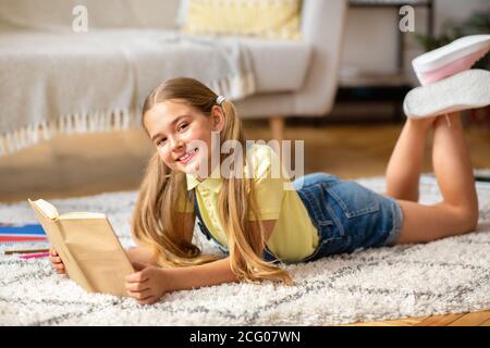 Girl lying on floor carpet, holding book, looking at camera Stock Photo