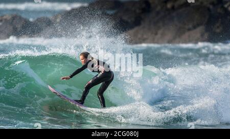 A panoramic image of spectacular surfing action as a young female surfer rides a wave at Fistral in Newquay in Cornwall. Stock Photo