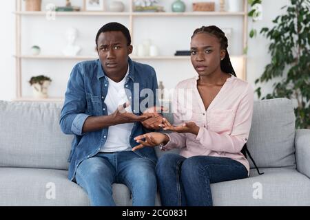 Frustrated Black Couple Sitting On Couch At Therapy Session, Looking With Misunderstanding Stock Photo