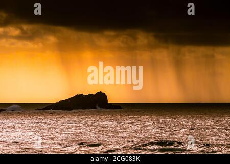 Rain clouds and a spectacular fiery sunset over Goose Island at Fistral in Newquay in Cornwall. Stock Photo