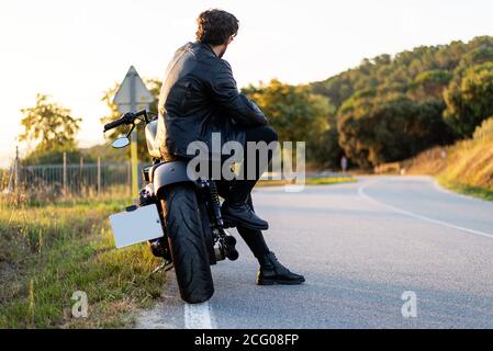 Rear view of bearded man sitting on a motorbike, while looking a¡way to road Stock Photo