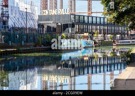 Regents Canal in London, UK with the moored canal boats and the Containerville premises in the background casting reflections on the water Stock Photo