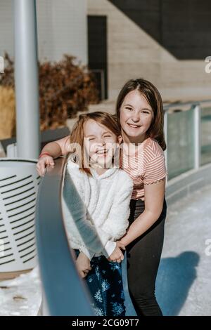 Happy young girls hugging on the side of ice skating rink Stock Photo