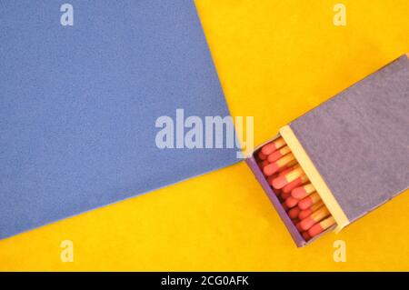 Matchbox, wooden, matchsticks with red head in a half-open box, on a blue and yellow background, with copy space Stock Photo