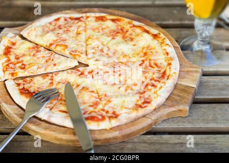 Freshly baked hot pizza Margarita on wooden board, close up. Cutlery, knife and fork, top view. Italian cuisine rustic style Stock Photo