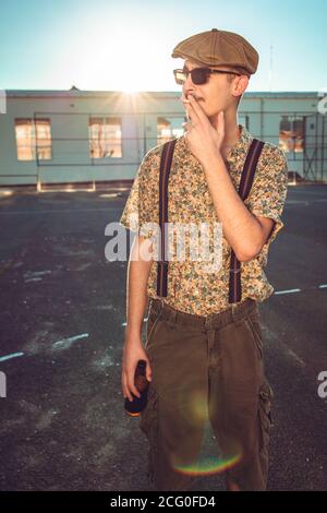 Young hipster man in retro clothing smokes while holding beer in hand Stock Photo