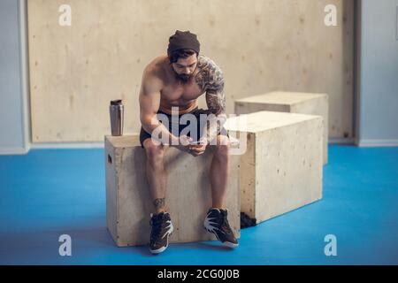 guy bodybuilder tired sit in gym and drink sportive nutrition - protein of shaker , vertical photo Stock Photo