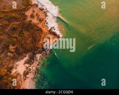 Aerial view of rocky shore with ocean waves and sunset tones. Stock Photo