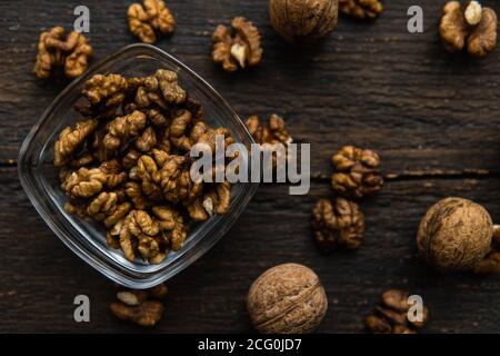 Walnut in a smale plate with scattered shelled nuts and whole nut which standing on a wooden vintage table. Walnuts is a healthy vegetarian protein Stock Photo