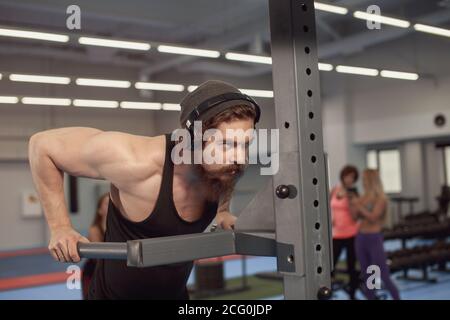 Strong tattooed in black unlabeled tank t-shirt male athlete shows calisthenic moves Holding dip position on parallel bars Stock Photo