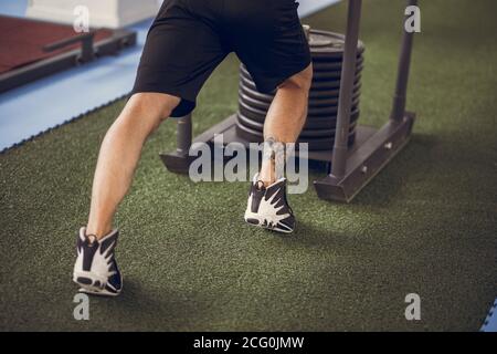 Strong man with muscular body pushing iron sled with weight in the gym. Cross fit and weightlifting. Stock Photo