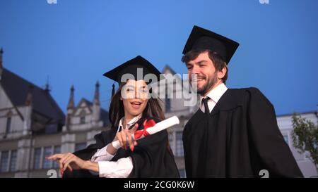 Happy young graduates dancing and celebrating graduation in park near academy. Stock Photo