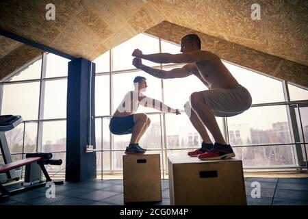 Male and female athletes doing box jumps at gym Stock Photo