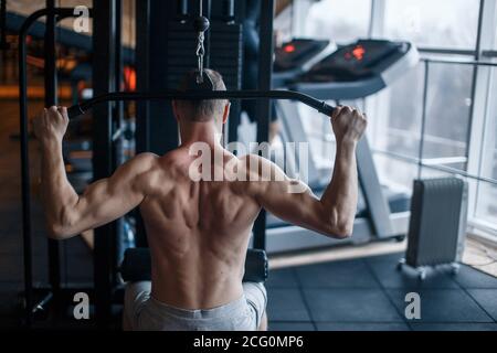 Shoulder pull down machine. Fitness man working out lat pulldown training at gym. Upper body strength exercise for the upper back. Stock Photo