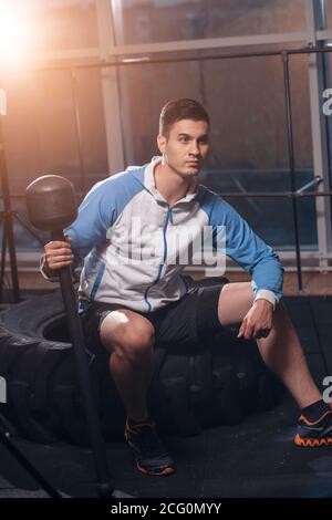 two Young man with a hammer strike on a tire in the gym. Workout. Stock Photo