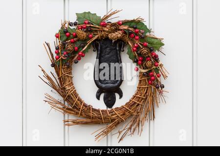 Detail of a Christmas wreath or garland on the cast iron knocker of a traditional painted wooden door Stock Photo