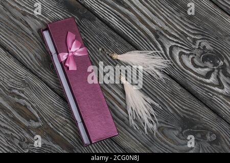 Ostrich feather brush earrings and a case for them. They lie on pine boards painted in black and white. Autumn gifts for loved ones. Stock Photo