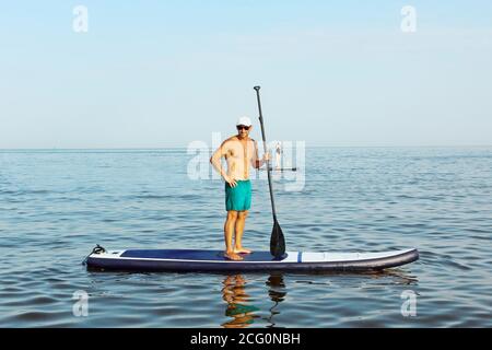 SAP Board surfing. Man is training on a SUP board in the blue sea. Stock Photo