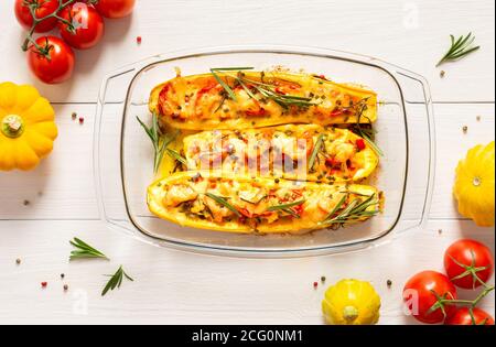 Stewed yellow zucchini with tomatoes and onions, cheese and herbs, carrots and spices, stuffed zucchini on a white wooden background Stock Photo