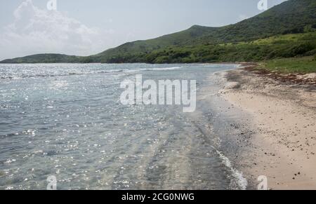 Glistening Caribbean Sea waters with remote sandy beach surrounded by rolling, green hills on St. Croix in the US Virgin Islands Stock Photo