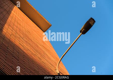 A deep red brick wall supports a lamppost, contrasting and bright colors. Stock Photo