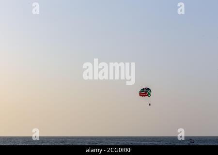 Parasailing in Dubai - single colorful parasail (parachute) tendem wing flying, towed behind a boat before sunset with orange and blue sky background. Stock Photo