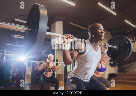 group of young athletes with African trainer doing squats with a barbell Stock Photo