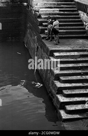 AJAXNETPHOTO. 1967. PORTSMOUTH, ENGLAND. - HOPING FOR A BITE - YOUNGSTERS WITH IMPROVISED FISHING TACKLE ON THE STEPS AT FLATHOUSE QUAY.PHOTO:JONATHAN EASTLAND/AJAX REF:356773 14 6 Stock Photo