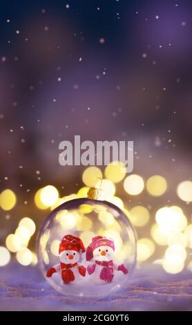 Christmas glass transparent ball with a snowmen inside on snow. Christmas lights glitter background. Stock Photo