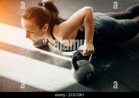 Slim brunette doing push-ups exercises on kettlebells. Cross fit training Stock Photo