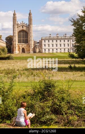 Woman sitting reading a book overlooking the backs and the meadows leading to kings collage Cambridge Cambridgeshire Stock Photo
