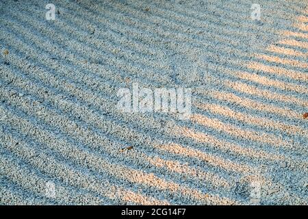 Sunshine ray on surface of gravel grooves symbolic rows in Gravel Stones Garden. Concentric lines of raked up white gravel in Japanese Zen Garden. Stock Photo