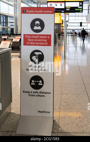 Public health notice giving instructions to passengers at Heathrow Airport to wear a mask, wash hands and keep a safe distance for Covid-19 pandemic Stock Photo