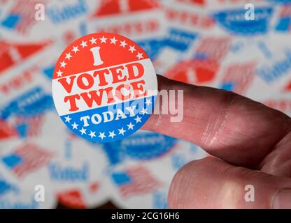 Finger with I Voted Twice button in front of many stickers given to US voters in Presidential election to illustrate vote fraud Stock Photo