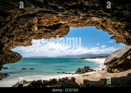 Pristine stretch of white secluded beach with alluring blue water, shot from big cave, beautiful sunny day Stock Photo
