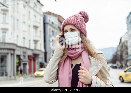 Concerned woman using her phone wearing medical mask and gloves Stock Photo